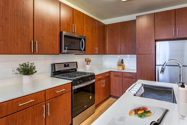 Newly renovated apartment homes feature kitchens with cherry cabinetry, white quartz countertops, stainless steel appliances, white tile backsplash, and hard surface flooring