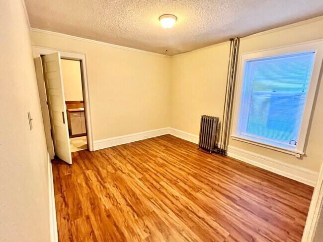 Disfrute de la comodidad de este acogedor dormitorio, que cuenta con elegantes suelos de madera y abundante luz natural. - Cross Apartments