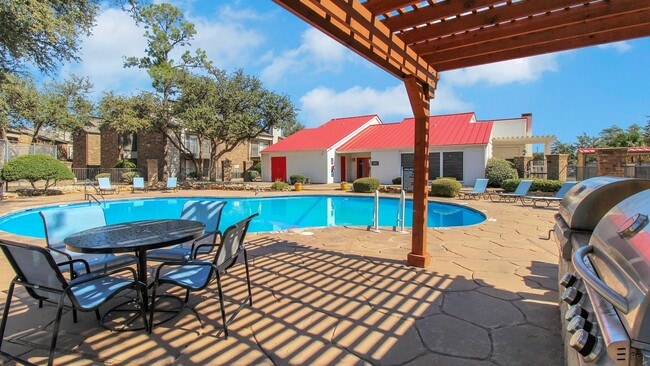 Inviting poolside view featuring modern patio furniture, vibrant landscaping, and charming clubhouse with a red roof. - Advenir at The Meadows