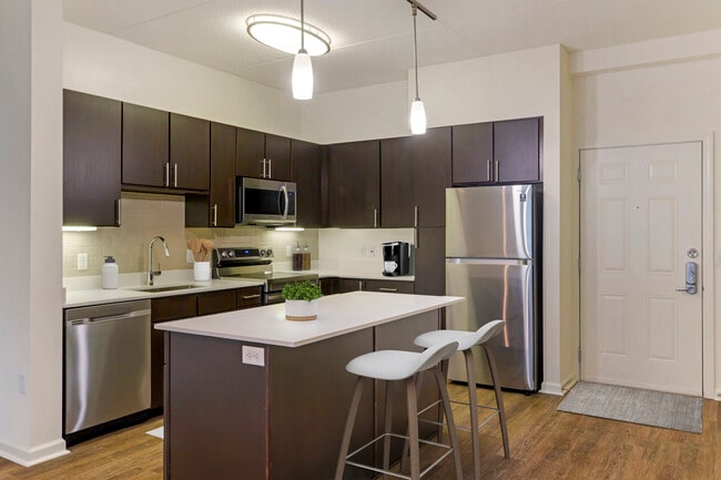 Renovated Package I kitchen with white quartz countertops, espresso cabinetry, stainless steel appliances, tile backsplash, and hard surface flooring throughout (in select homes)