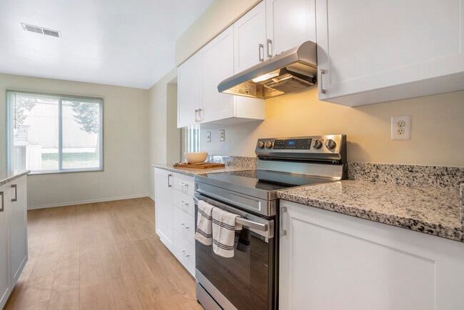 Renovated Package II kitchen featuring stainless steel appliances, white cabinetry, white speckled granite countertops, and hard surface flooring - eaves Tysons Corner Apartments