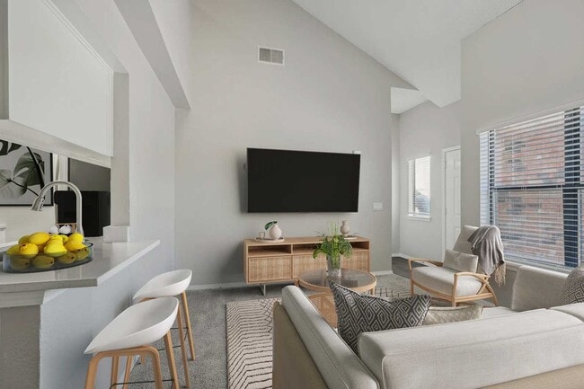 Open living area with vaulted ceiling, wall-mounted TV, rattan media console, gray sofa, and kitchen bar seating