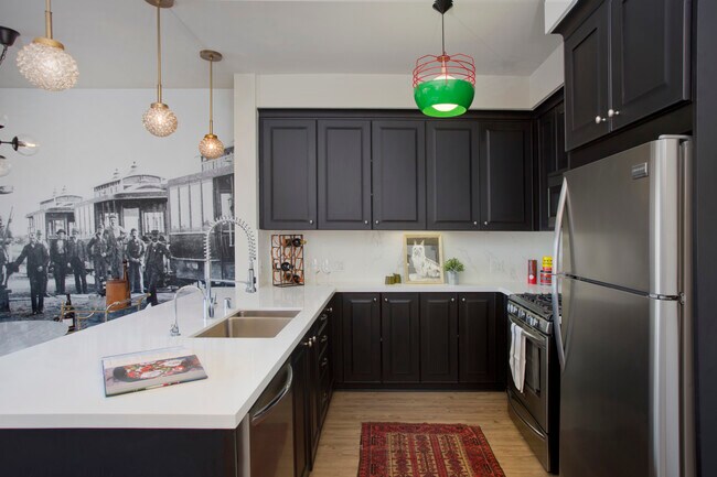 Kitchens with dark cabinetry, white quartz countertops, white tile backsplash, stainless steel appliances, and hard surface flooring - AVA Balboa Park Apartments