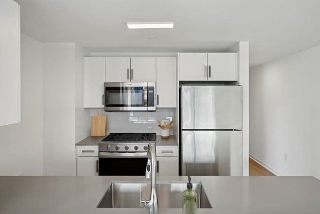Renovated Package I kitchen with stainless steel appliances, white cabinetry, tile backsplash, grey quartz countertops, and hard-surface flooring