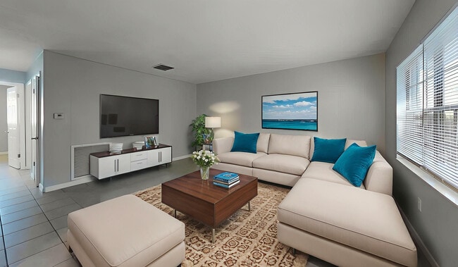 Modern living room featuring plush beige sectional sofa with vibrant teal cushions, chic wooden coffee table, wall-mounted TV, and large window for natural light. - Sunny Point Apartments
