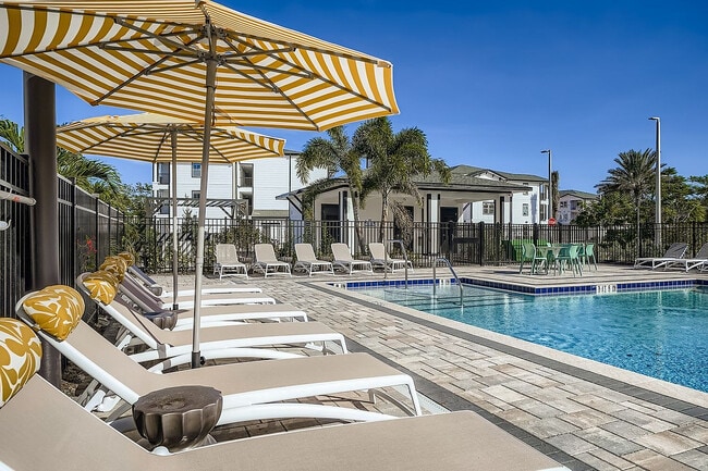 Premium outdoor pool area with elegant sun loungers, striped umbrellas, and lush greenery, perfect for relaxation and leisure.