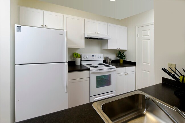 Kitchen with white appliances, white cabinetry and black countertops - eaves Fairfax City