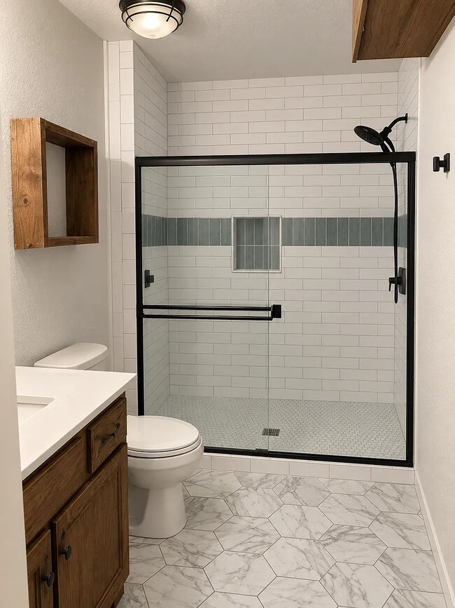 Completely renovated primary bath with glass-door walk-in shower and storage.