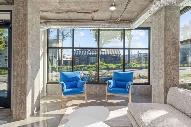This bright living room features comfortable blue couches, large windows that allow natural light, and a spacious layout.