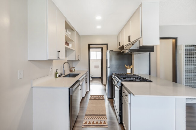 Renovated Package I kitchen with stainless steel appliances, white quartz countertops, white cabinetry, and hard surface flooring (select homes)