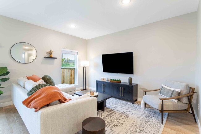 Bright and inviting living room with a cozy sofa, stylish accent chair, modern decor, and large flat-screen TV, ideal for relaxation and entertainment. - Summerwell Maple Grove