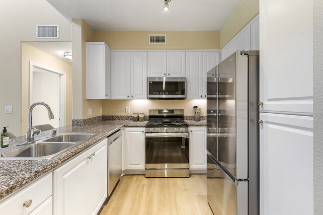 Renovated Package I kitchen with stainless steel appliances, beige speckled granite countertop, white cabinetry, and hard surface flooring - Avalon Glendale Apartments