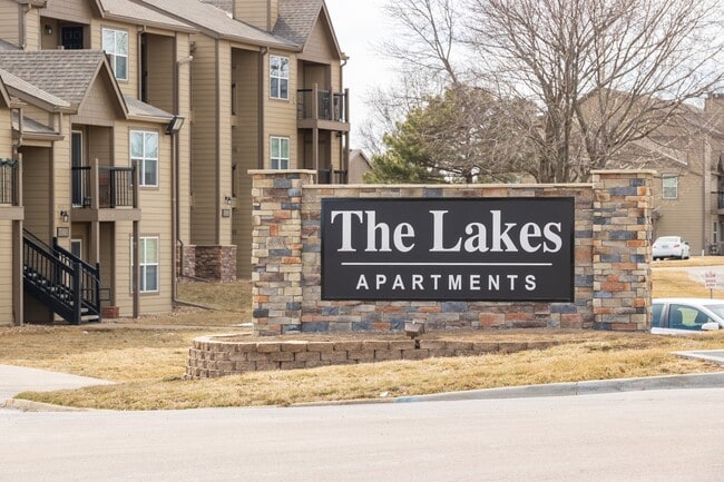 The Lakes community entrance features distinctive stone-brick signage with the apartment buildings visible in the background.
