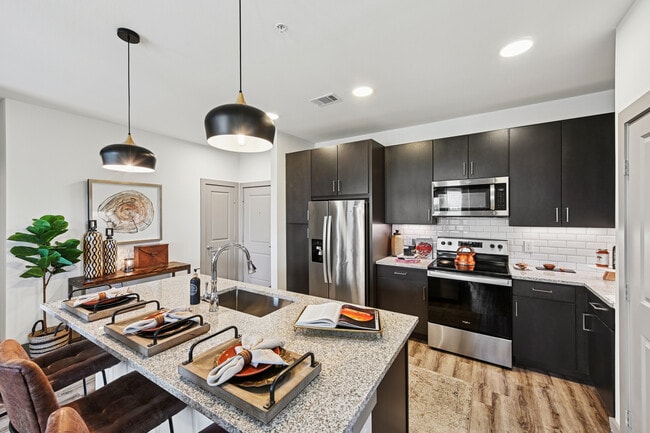 Cocina con gabinetes color espresso, encimeras de granito moteado, protector contra salpicaduras de azulejos blancos tipo metro, electrodomésticos de acero inoxidable y pisos de superficie dura. - Avalon Benbrook