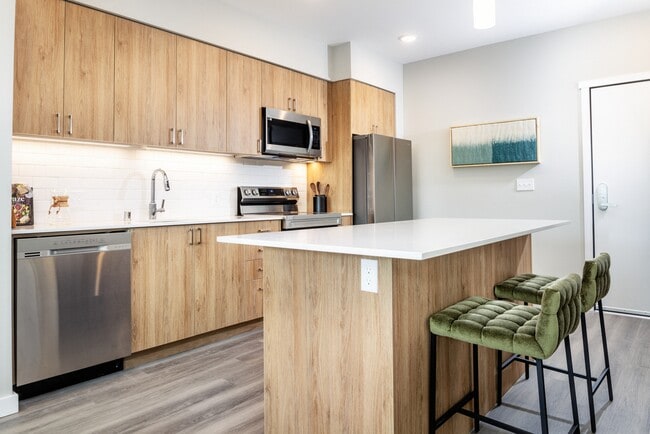 Kitchen with oak cabinetry, white granite countertops, white tile backsplash and stainless steel appliances - Avalon Redmond Campus Apartments