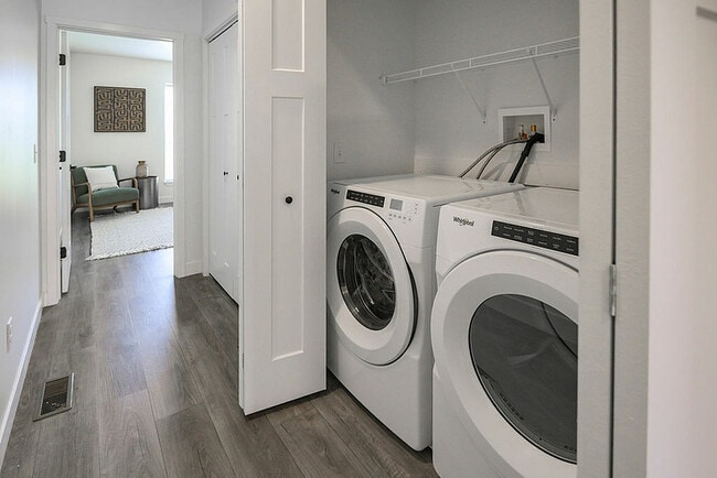 Área de lavandería moderna con elegantes unidades de lavadora y secadora, complementadas con elegantes pisos de madera y una vista de una habitación acogedora y elegante.