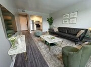 Open living and dining area with black sofa, marble table, green chair, wall art and kitchen with stainless appliances