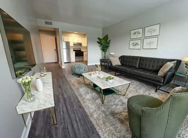 Open living and dining area with black sofa, marble table, green chair, wall art and kitchen with stainless appliances