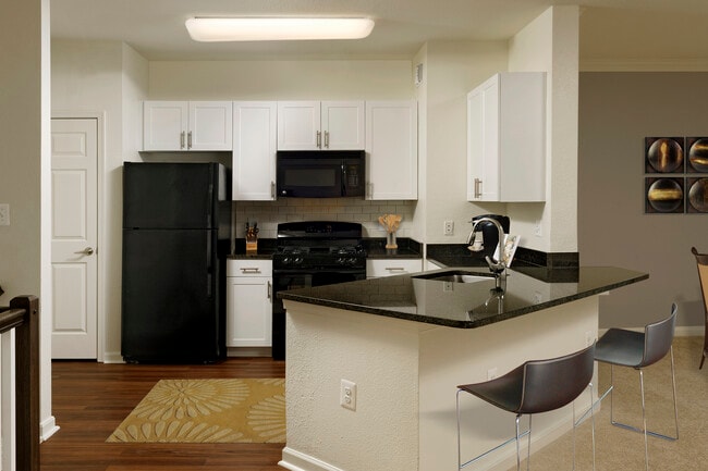 Renovated Package II kitchen with white cabinetry, black granite countertops, black appliances, white tile backsplash, and hard surface plank flooring