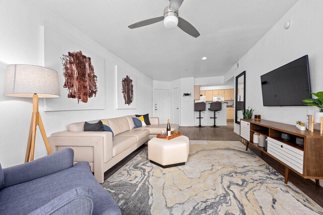 Living room with beige sectional, ceiling fan and wall-mounted TV on hardwood floors