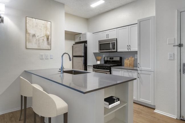 Renovated Package III kitchen with grey quartz countertops, white cabinetry, stainless steel appliances, tile backsplash, and hard surface plank flooring - Avalon Cove Apartments