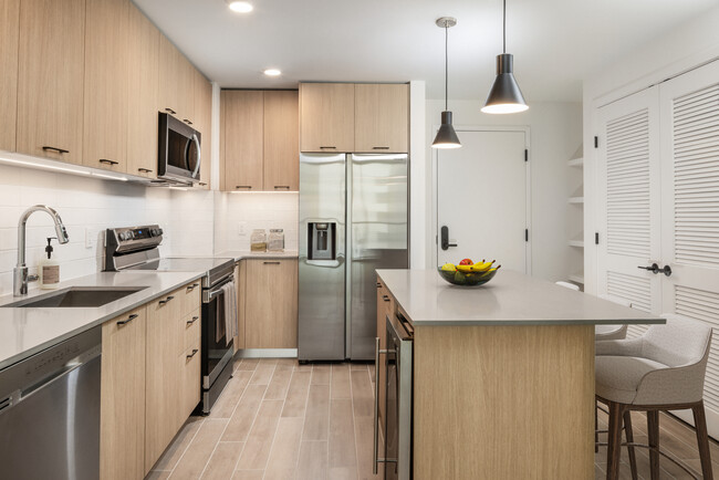 Cocina con electrodomésticos de acero inoxidable, encimeras de cuarzo gris, salpicadero de azulejos blancos y suelos de superficie dura - Avalon Merrick Park Apartamentos