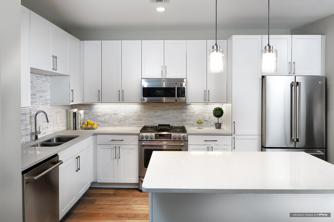 Signature Collection kitchen with white cabinetry, light grey quartz countertops, white marbled subway tile backsplash, stainless steel appliances, and hard surface flooring - Avalon Rockville Centre Apartments