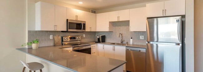 Limited availability: newly renovated Finish Package II apartment homes featuring kitchens with grey quartz countertops, white cabinetry, stainless steel appliances, grey tile backsplash, and hard surface flooring - Avalon Sunset Towers Apartments