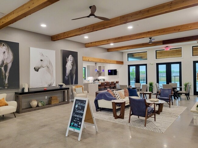 Open-concept clubhouse with lounge seating, kitchen bar, horse artwork, and pool views through large glass doors
