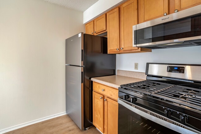 Renovated Package I kitchen with stainless steel appliances, laminate countertops, oak cabinetry, and hard surface flooring - eaves Fair Lakes