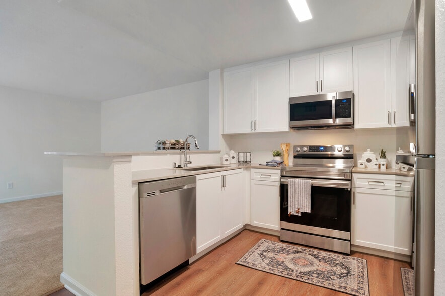 Kitchens with stainless steel appliances, beige quartz countertops, white cabinetry, and hard surface flooring