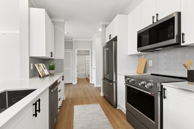 Renovated Package II kitchen with stainless steel appliances, white cabinetry, grey tile backsplash, white quartz countertops, and hard surface flooring