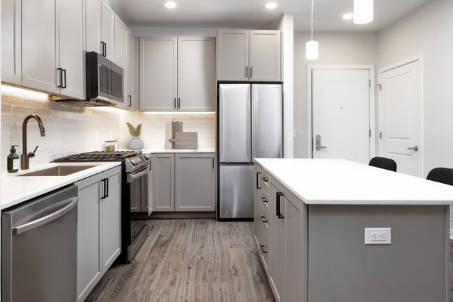 Coming Soon - New West Phase apartments - Finish Package IV Kitchen with stainless steel appliances, white quartz countertops, grey cabinetry, pendant lighting, and hard surface flooring (Representative photo) - Avalon Hunt Valley Apartments