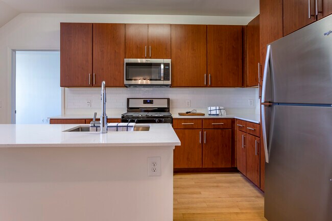 Newly renovated apartment homes feature kitchens with cherry cabinetry, white quartz countertops, stainless steel appliances, white tile backsplash, and hard surface flooring