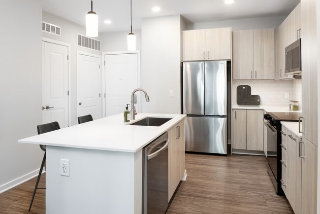 Design Collection II kitchen with stainless steel appliances, cream quartz countertops, oak cabinetry, and hard surface flooring