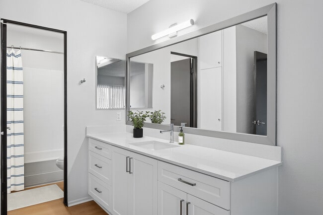 Renovated Package II bath with white quartz countertops, white cabinetry, updated hard surface flooring, and framed mirror