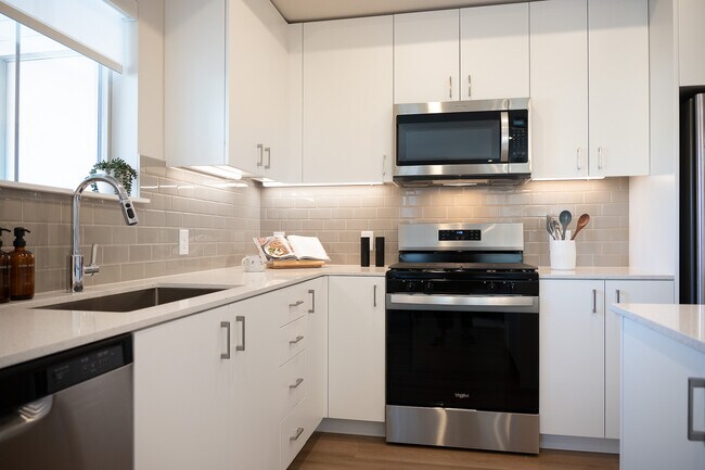 Finish Package I kitchen with stainless steel appliances, white cabinetry, grey tile backsplash, white quartz countertops, and hard surface flooring - Avalon Parker