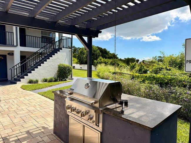 Charming outdoor area featuring a sleek stainless steel grill under a stylish pergola, surrounded by lush greenery and a cozy patio setting. - Waterside Village