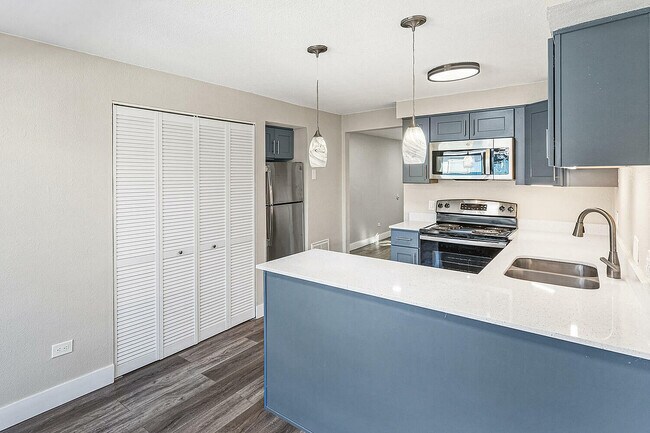 Modern kitchen with sleek blue cabinetry, stainless steel appliances, and elegant pendant lighting in a sunlit apartment.