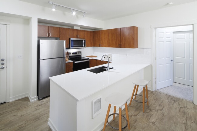 Renovated Package I kitchen with white quartz countertops, oak cabinetry, stainless steel appliances, tile backsplash, and hard surface flooring - Avalon Bellevue Apartments