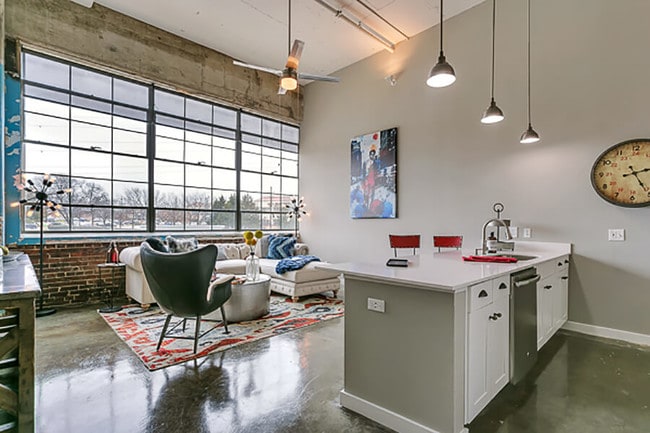 Sala de estar con cocina de concepto abierto, pisos de hormigón, y hermosos gabinetes de color blanco. Apartamento estilo loft - Lofts at Mockingbird Station Apartments