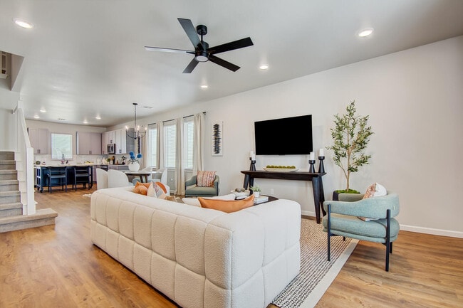 Open living room with sectional sofa, accent chairs, ceiling fan, and view toward kitchen and dining area