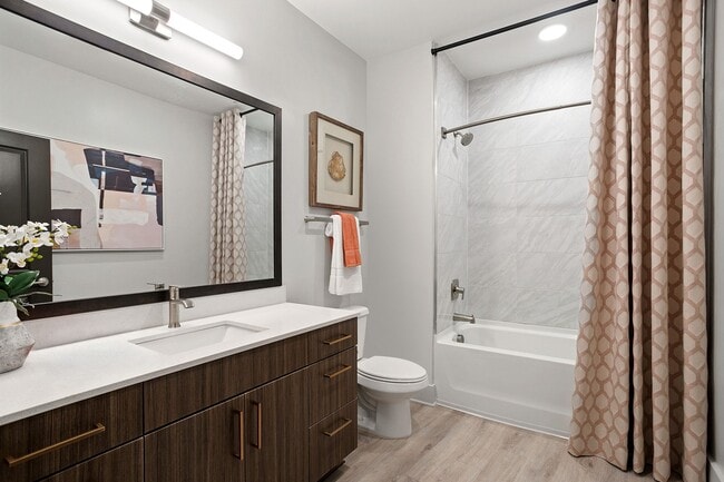 Modern bathrooms with framed mirrors, curved shower rods and quartz countertops - Auden Apartments