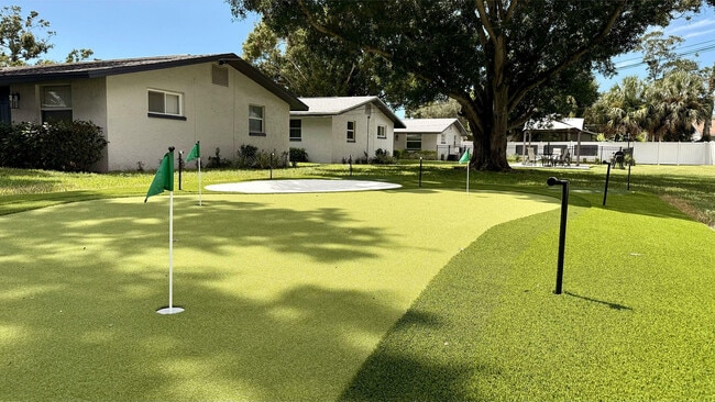 Idyllic backyard featuring a lush putting green, shaded by a grand tree, perfect for golfing enthusiasts and relaxation.