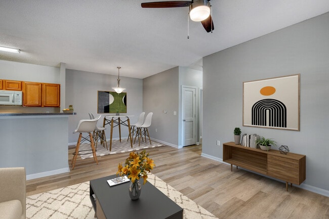 Spacious living and dining area at Dunwoody Place with an open layout, light wood flooring, contemporary furniture, and access to a private patio or balcony in an income-restricted apartment community in Huntsville, Alabama. - Dunwoody Place