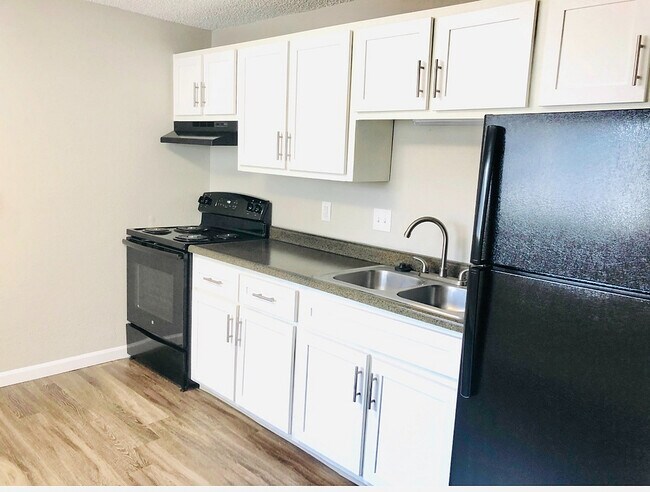 Modern kitchen with sleek black appliances, stylish white cabinetry, and elegant wood flooring.