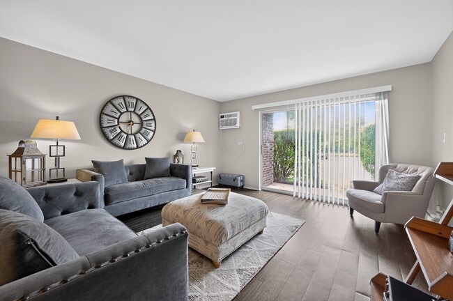 Gather in a comfortable living room featuring grey couches and a statement wall clock at Renaissance at Carol Stream in Carol Stream, IL.