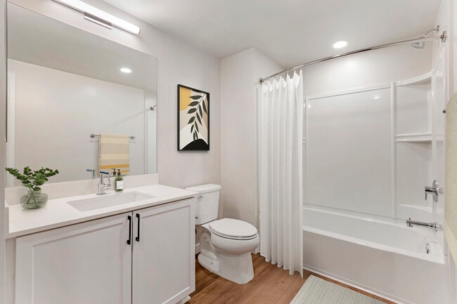 Renovated Package II bath with white quartz countertops, white cabinetry, and hard surface flooring - Avalon Wilshire
