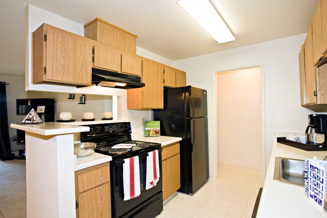 Kitchen with oak cabinetry, white countertops, black appliances and tile flooring