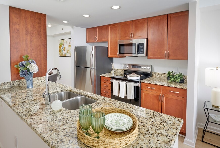 Newly Renovated Ellington Floor Plan Kitchen at Meridian at Grosvenor Station featuring sleek stainless steel appliances, modern vinyl plank wood-style flooring, and updated lighting fixtures that complement existing granite countertops and custom cabinetry.